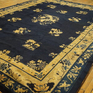 Dark blue area rug with detailed gold and beige floral patterns and borders on a rustic wood floor.
