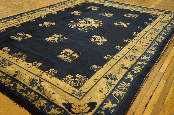 Dark blue area rug with detailed gold and beige floral patterns and borders on a rustic wood floor.