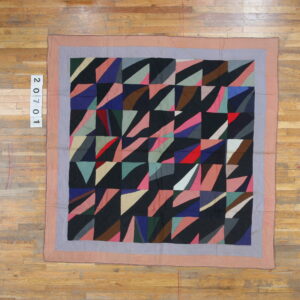 A flat, multicolored geometric textile with mauve and gray borders resting on light plank wood flooring.