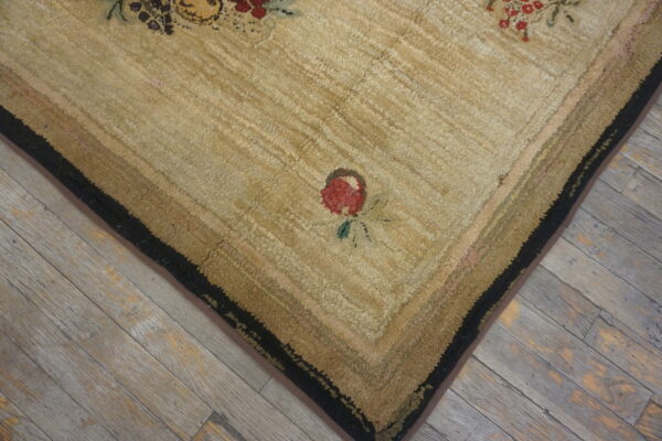 Textured beige rug corner shows a red floral motif, striped borders, and a black edge on distressed wood.
