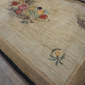 Textured beige rug with colorful hooked floral and fruit designs lying on gray wooden floorboards.