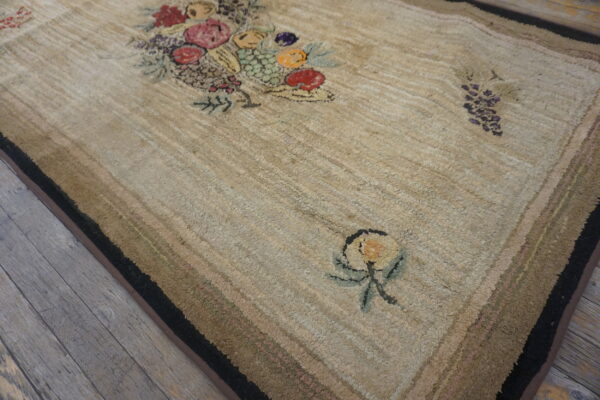 Textured beige rug with colorful hooked floral and fruit designs lying on gray wooden floorboards.
