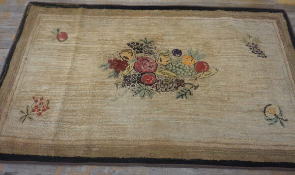Textured beige area rug with a multicolored fruit basket center and layered brown and black borders.