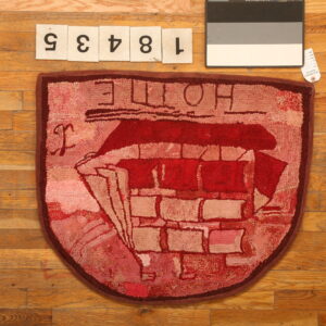 Shield-shaped hooked rug in deep red and pink colors with a stylized boat motif on wood.