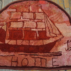 D-shaped, textured red rug depicting a tall ship and the word HOME on weathered wood planks.