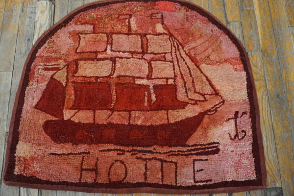D-shaped, textured red rug depicting a tall ship and the word home on weathered wood planks.