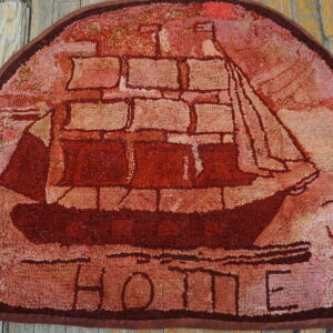 Rustic red hooked rug showing a sailing ship and the word HOME on weathered wood flooring.