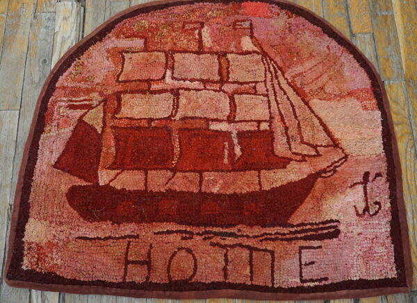 Rustic red hooked rug showing a sailing ship and the word home on weathered wood flooring.