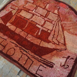 Red and pink hooked rug featuring a sailboat pattern and the word HOME on distressed wood flooring.