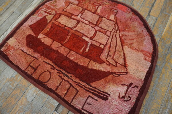 Red and pink hooked rug featuring a sailboat pattern and the word home on distressed wood flooring.