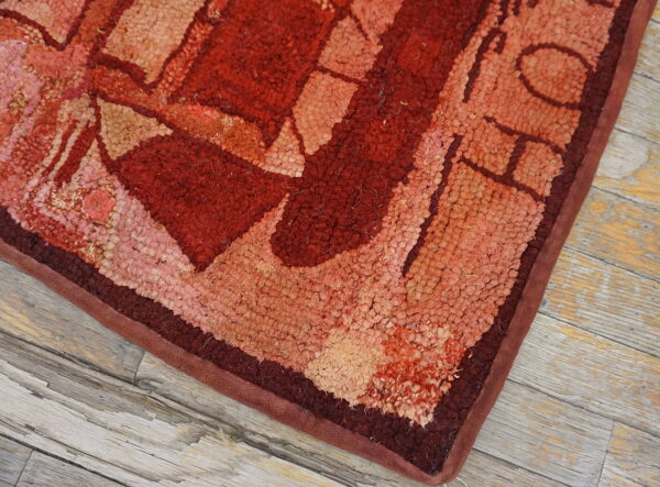 Textured rug corner displaying abstract shapes in reds and tans, resting on distressed gray wood.