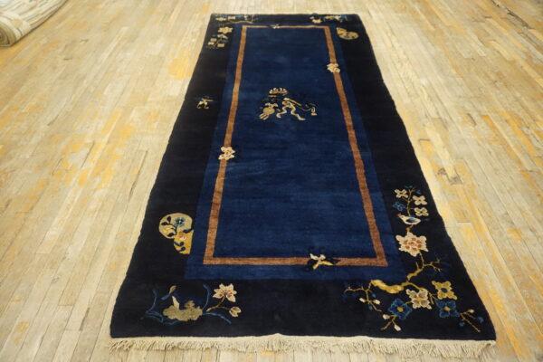 Deep blue runner rug with tan trim and multicolored floral designs lying on distressed hardwood planks.