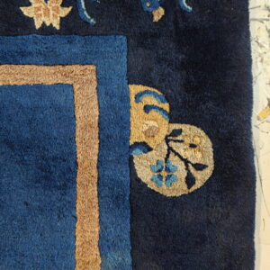 High-pile navy rug detail featuring a tan and blue border with stylized creature and floral motifs.