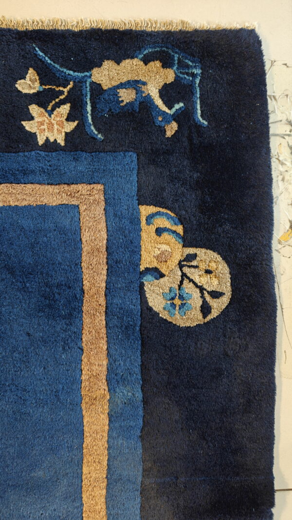 High-pile navy rug detail featuring a tan and blue border with stylized creature and floral motifs.
