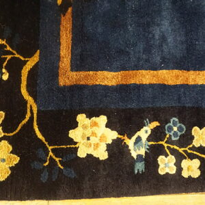 Detail view of a navy blue rug featuring gold vines, yellow and blue flowers, and a detailed tan border.
