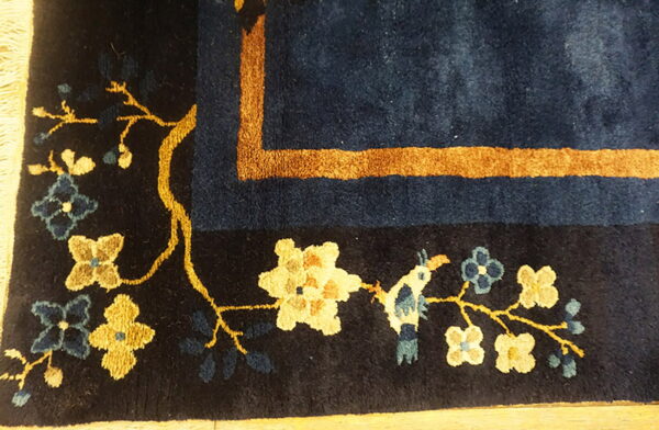 Detail view of a navy blue rug featuring gold vines, yellow and blue flowers, and a detailed tan border.