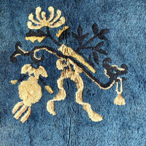 Close-up of a blue plush rug featuring a gold and navy stylized floral pattern.