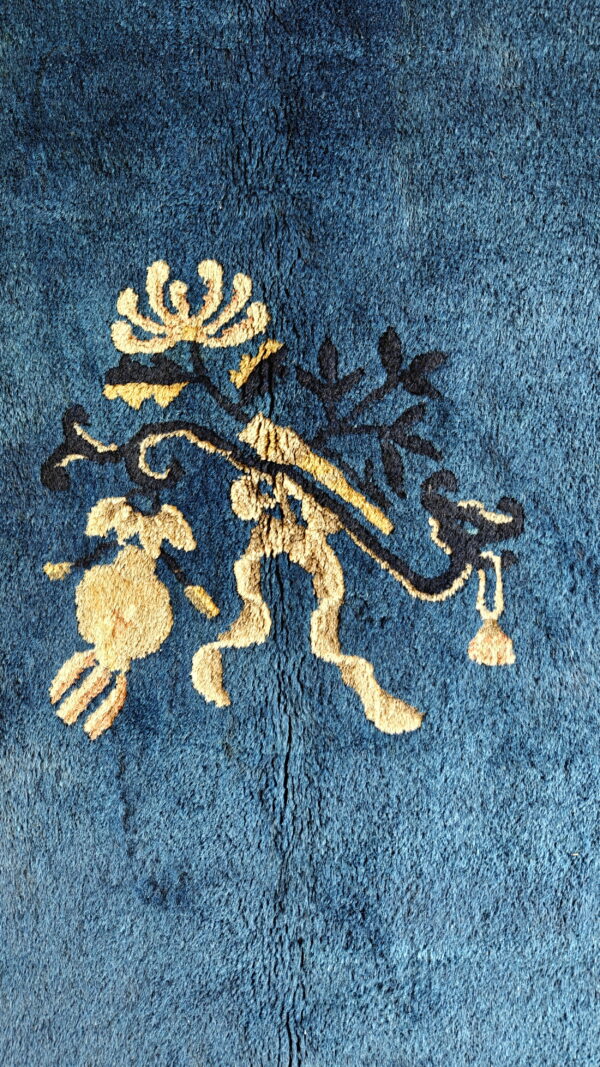 Close-up of a blue plush rug featuring a gold and navy stylized floral pattern.