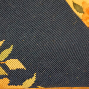 Close-up of a rug revealing the dark blue flatwoven backing and bright orange, yellow, and green floral face.
