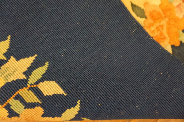 Close-up of a rug revealing the dark blue flatwoven backing and bright orange, yellow, and green floral face.