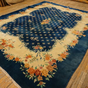 Large teal blue rug with a cream medallion defined by orange and pink floral garlands on wood flooring.