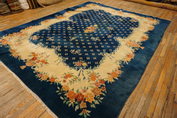 Large teal blue rug with a cream medallion defined by orange and pink floral garlands on wood flooring.