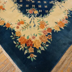 Blue floral rug corner showing an ivory field and orange flowers against rustic wood floors.