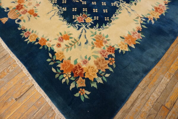 Blue floral rug corner showing an ivory field and orange flowers against rustic wood floors.