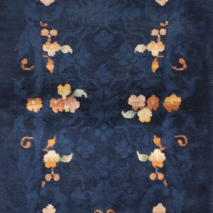 High-pile navy rug features tone-on-tone scrolling and symmetric bouquets of orange, yellow, and peach floral designs.