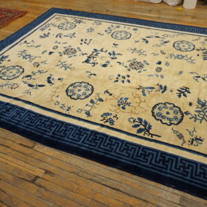 Cream and blue rug with floral designs and a wide geometric border lies on rustic wooden flooring.