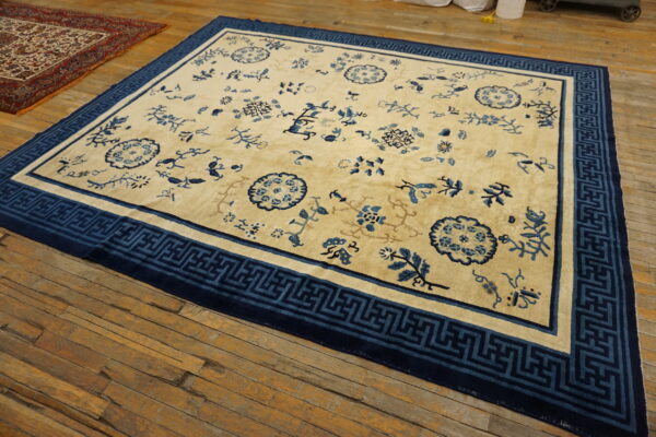 Cream and blue rug with floral designs and a wide geometric border lies on rustic wooden flooring.