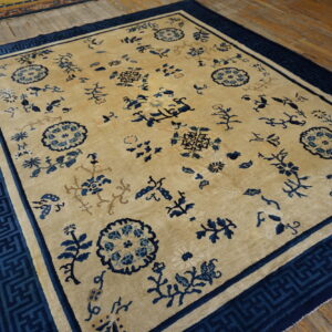 Light beige rug with scattered dark blue floral designs and a wide geometric border on wooden floors.