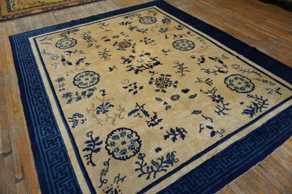 Light beige rug with scattered dark blue floral designs and a wide geometric border on wooden floors.