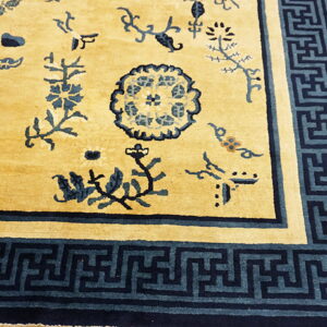 Close-up of a golden yellow rug featuring scattered blue floral motifs and a geometric key border on wood flooring.