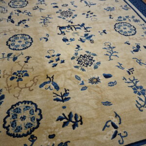 A beige rug with scattered blue floral and medallion patterns, featuring a dark blue geometric key border.