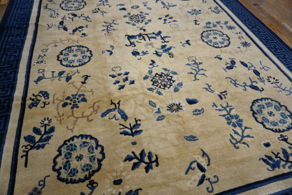 A beige rug with scattered blue floral and medallion patterns, featuring a dark blue geometric key border.