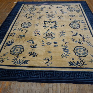 Yellowish-tan rug with scattered blue patterns and a geometric Greek key border on wood planks.