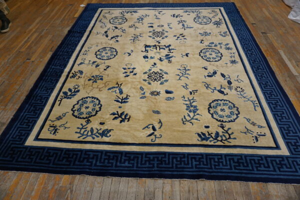 Yellowish-tan rug with scattered blue patterns and a geometric greek key border on wood planks.