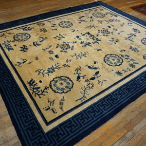 Tan rug with scattered blue floral patterns and a wide, dark blue geometric border on wood flooring.