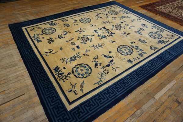 Tan rug with scattered blue floral patterns and a wide, dark blue geometric border on wood flooring.