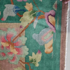 Close-up of a teal rug with multicolored pink and yellow floral patterns and a low, textured pile.