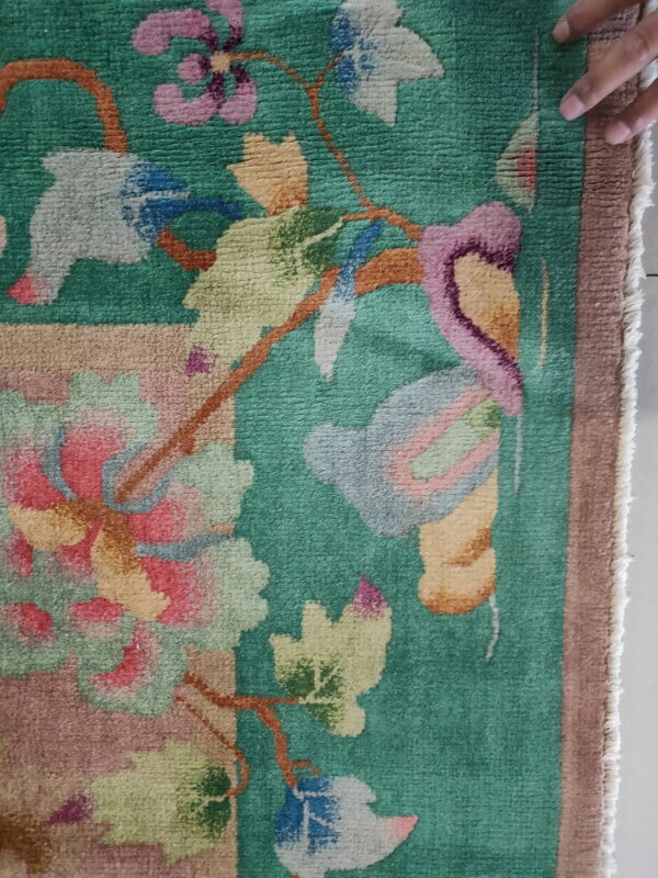 Close-up of a teal rug with multicolored pink and yellow floral patterns and a low, textured pile.