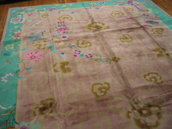 Low-pile rug with a rose field, scrolling patterns, a teal border, and multicolored flowers on wood flooring.