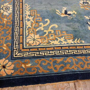 Blue rug detail shows intricate tan, cream, and navy geometric and floral borders on wood planks.