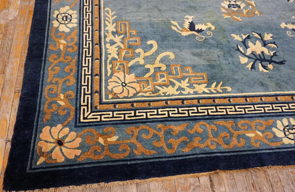 Blue rug detail shows intricate tan, cream, and navy geometric and floral borders on wood planks.