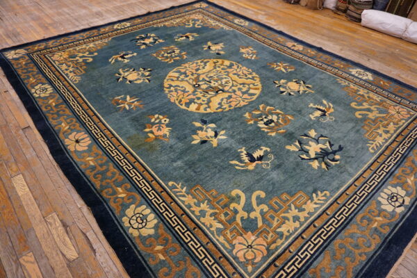 Teal and gold rug with a complex floral medallion and geometric borders on distressed wood floor.