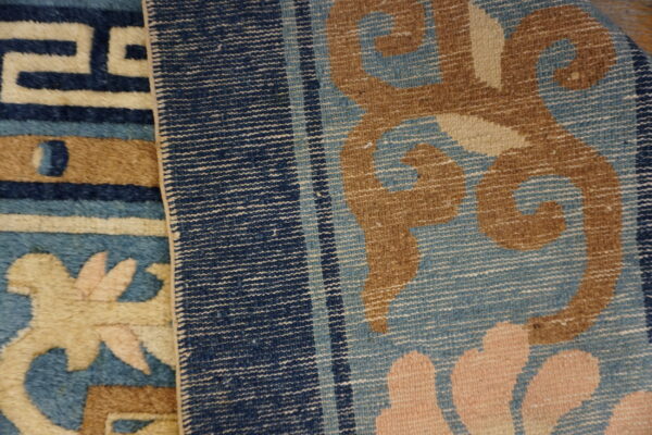 Detail of two rugs; one plush blue/tan geometric pattern and one striped flatweave with large floral motifs.