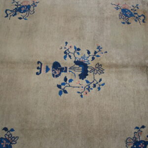 Low-pile rug in dusty beige with stylized blue and pink floral patterns.