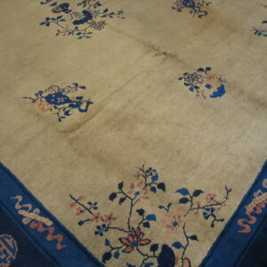 Pale tan rug with scattered blue and peach floral sprays and a wide, dark blue border.