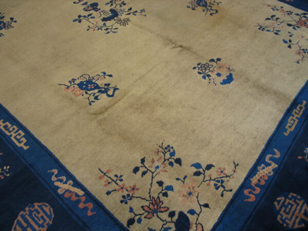 Pale tan rug with scattered blue and peach floral sprays and a wide, dark blue border.
